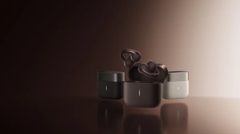 Photo of the Anker Soundcore AeroClip 2 Pro earbuds. A render of the brown earbuds above an open case in front of one black and one white case. Background is a dramatic, monochrome spotlight gradient.