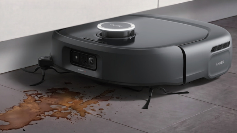 Photo of the Eufy Robot Vacuum Omni E35. A black robot vacuum works on a spill of brown liquid on a dark gray tile floor.