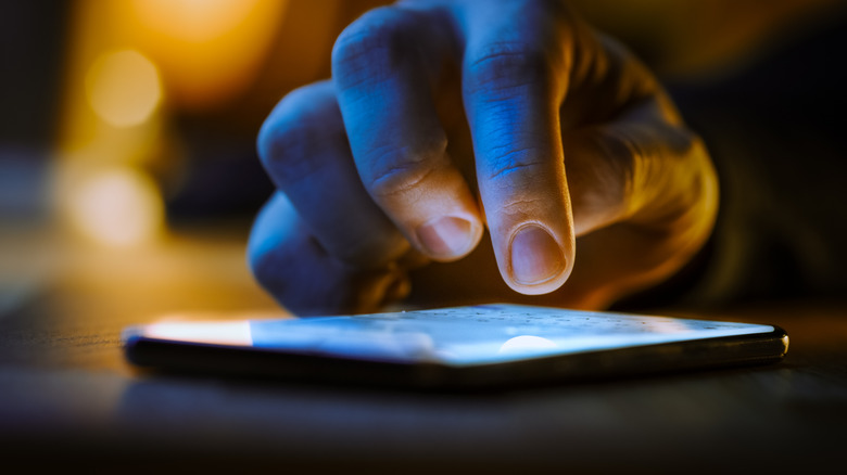 Photo showing a close-up of a hand about to touch a glowing smartphone screen
