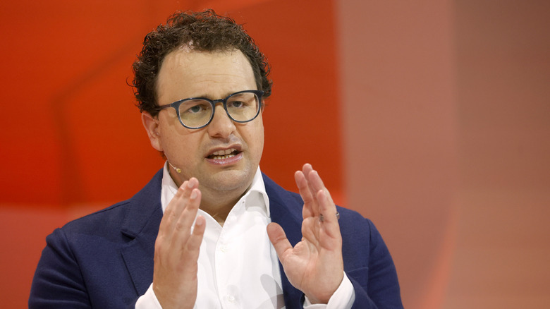 Anthropic CEO Dario Amodei speaks in front of an orange backdrop, hands lifted by his chin.