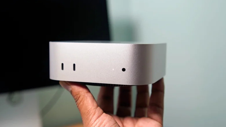 A hand holding a silver M4 Pro Mac mini.