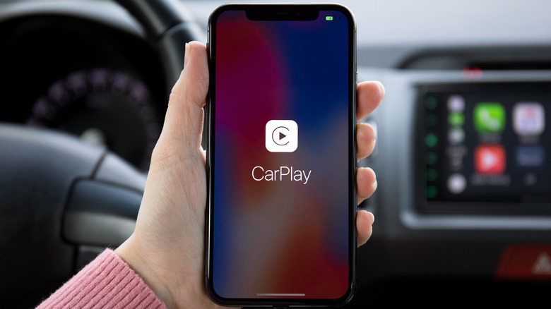 Hand holding iPhone in a car with the CarPlay logo on the screen
