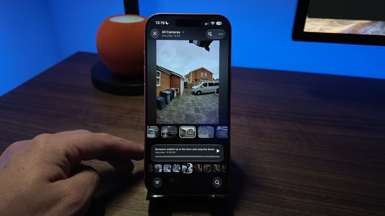 Apple's Home app shows a video of a driveway behind a brown house, where a van pulls up and an AI video description states that someone is about to walk to the front door.