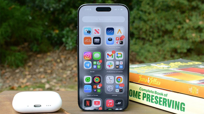 An iPhone 17 sits next to an AirPods Pro case and a couple of books.
