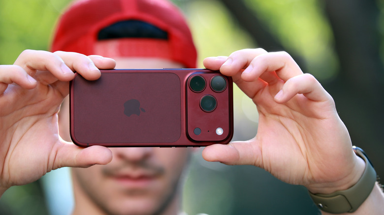 A person holding up the burgundy iPhone 18 Pro horizontally to take a picture.