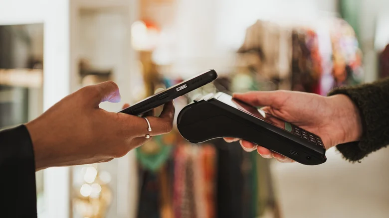 A smartphone being used to make a payment using tap-to-pay against a portable contactless terminal.
