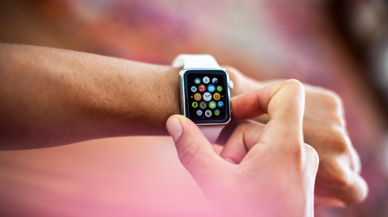 An arm held up with an Apple Watch on the wrist, as the other hand presses the side button.