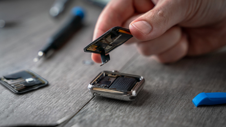 A person removing the case from an Apple Watch using a kit to replace the battery.