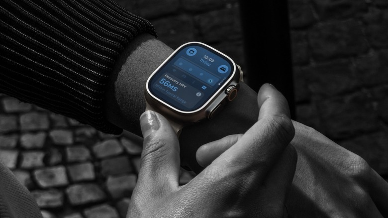 Close-up photo of an Apple Watch Ultra 4. A mostly black-and-white image of a wearer framing the color screen of the smartwatch on their wrist.
