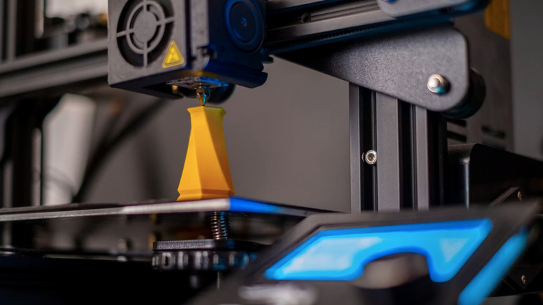 A 3D printer making a small, yellow twisted vase.