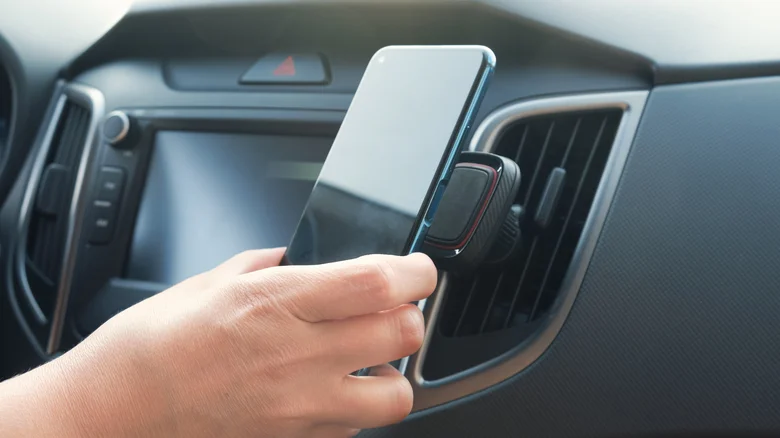 Hand placing a smartphone into a car air vent mount.