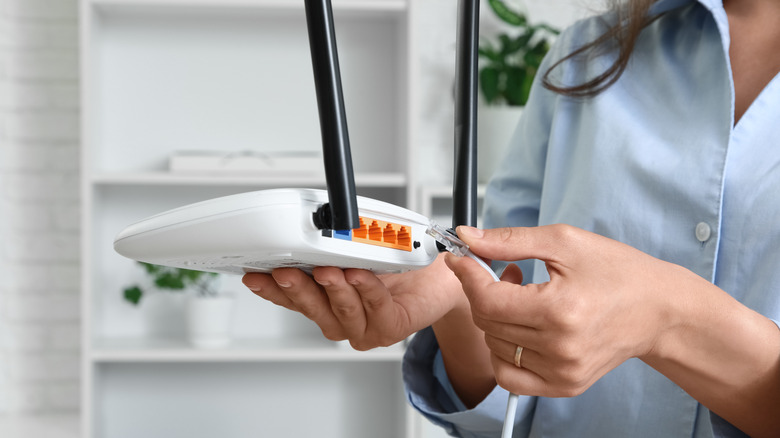 Person connecting an Ethernet cable to the back of a wireless router.