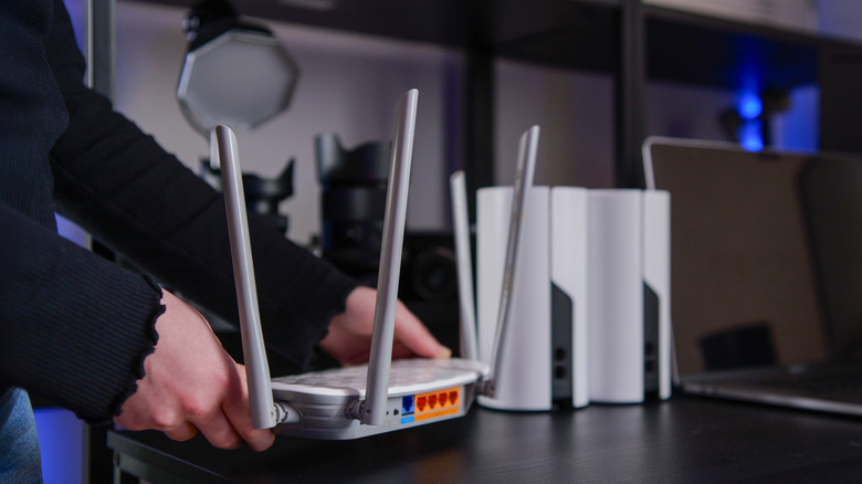 Person setting up a Wi-Fi router beside several mesh network nodes.