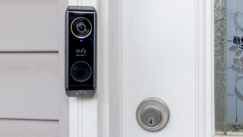 eufy video doorbell mounted on a white door frame beside a door lock.