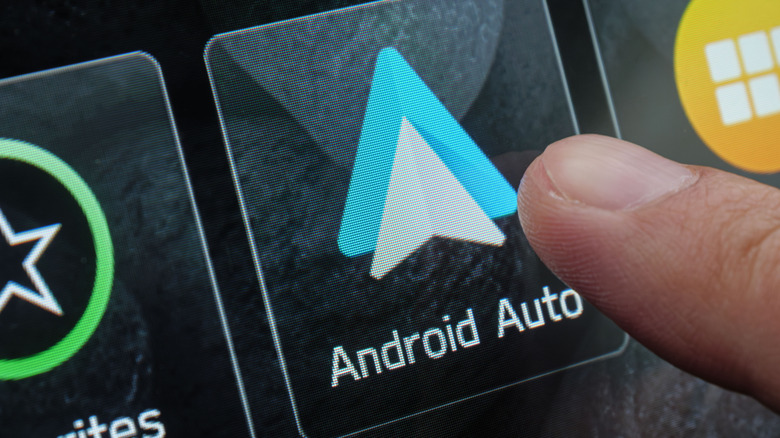 A finger tapping an Android Auto button on a car touchscreen.