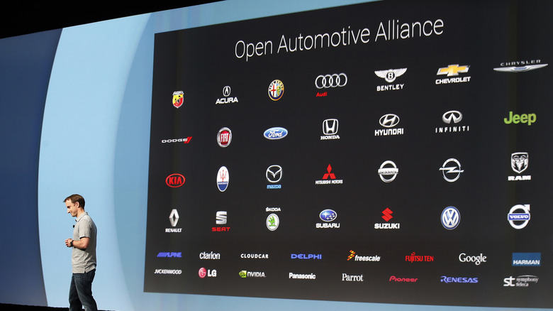 Google executive Patrick Brady discusses the Open Automative Alliance on-stage, with a large backdrop showing companies that support the initiative