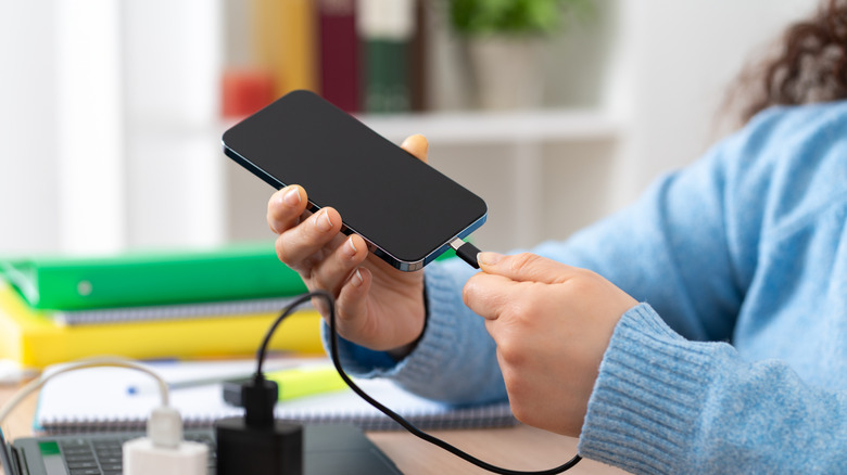 A woman holding a phone and plugging a charging cable into it.