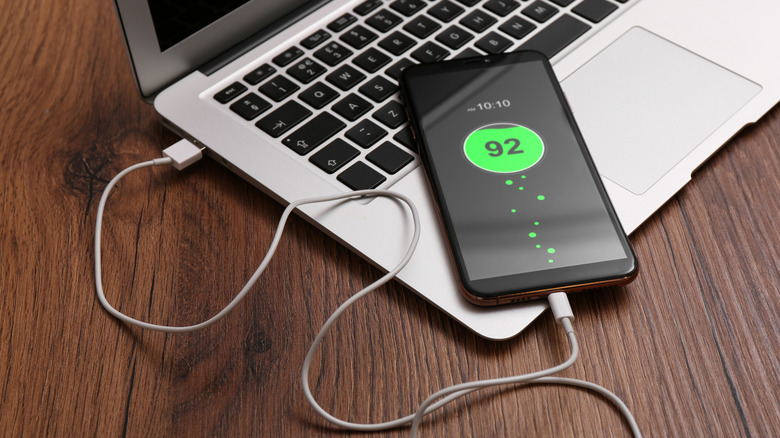 A phone plugged into a laptop, charging.
