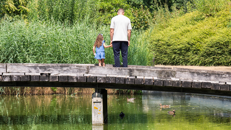 Photo of a father and daughter on a cute wooden bridge in Paris with ducks underneath