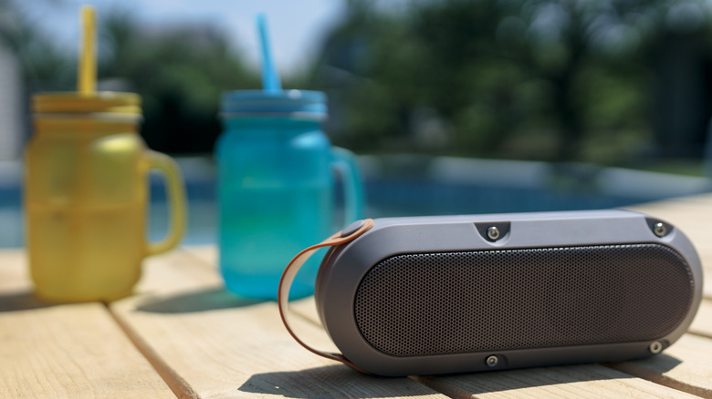 A Bluetooth speaker sitting next to two drinks by a pool