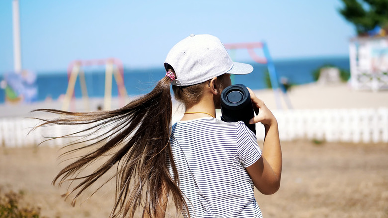A young woman holding a Bluetooth speaker at the beach