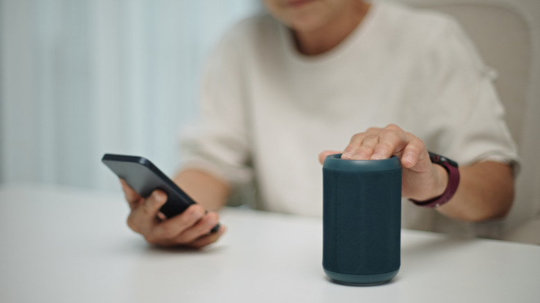 A person holding buttons on their Bluetooth speaker to pair with their phone