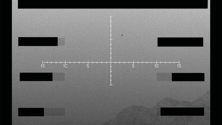 A black and white photo of a black speck floating over a mountain range.