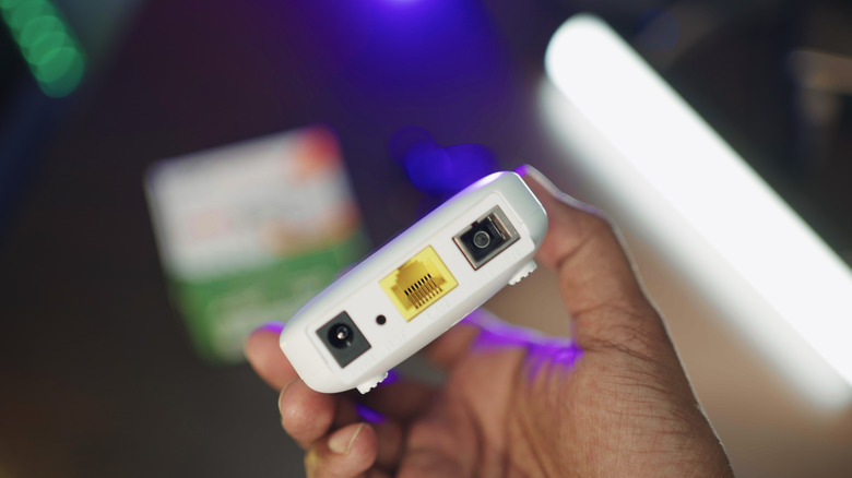 Person holding a compact white router with an Ethernet port.
