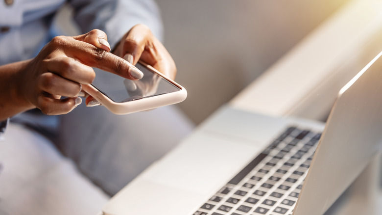 Person using a smartphone beside an open laptop.