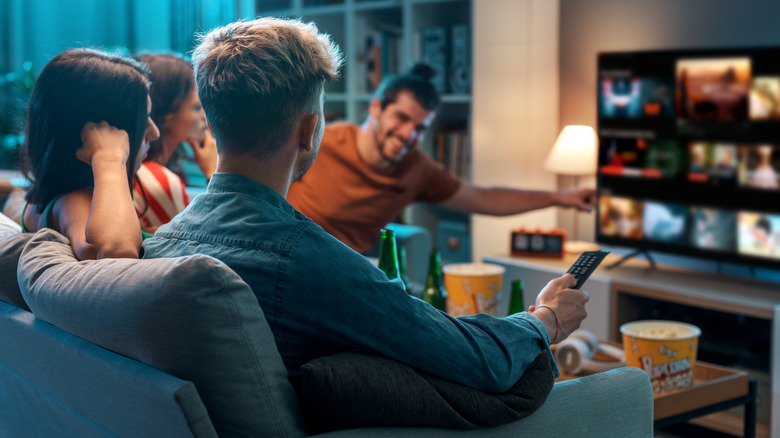 Four friends in a living room choosing a movie on TV, one holding a remote.