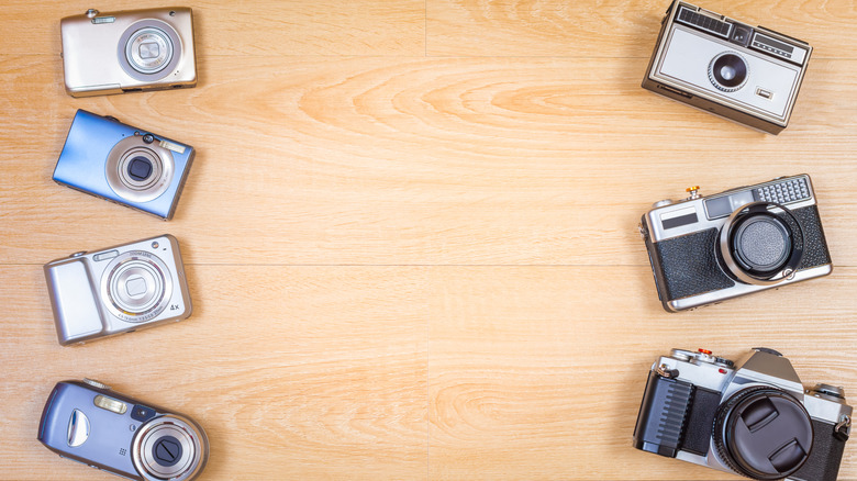 Several cameras arranged around the edges of a wooden table.