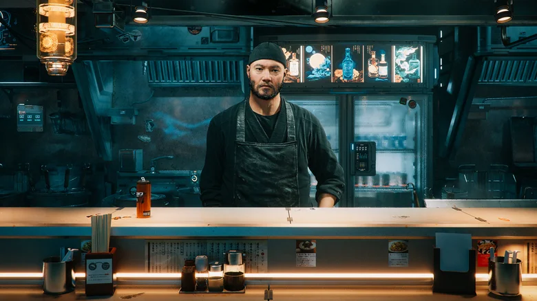 A man stands at a food truck counter, staring at the customer.