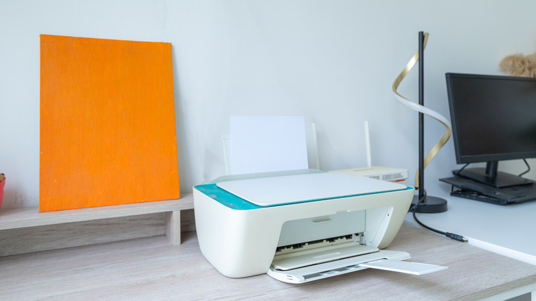 Printer on desk next to a Wi-Fi router and other equipment.