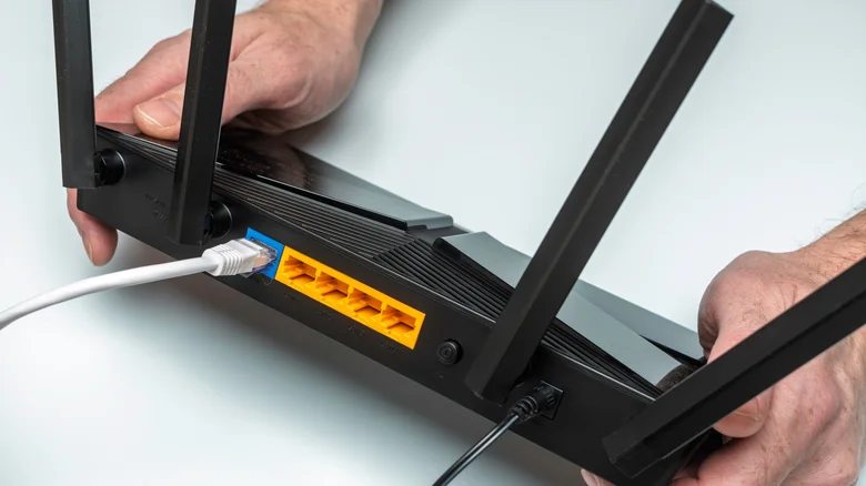 Person showing the rear of a router with cables connected.