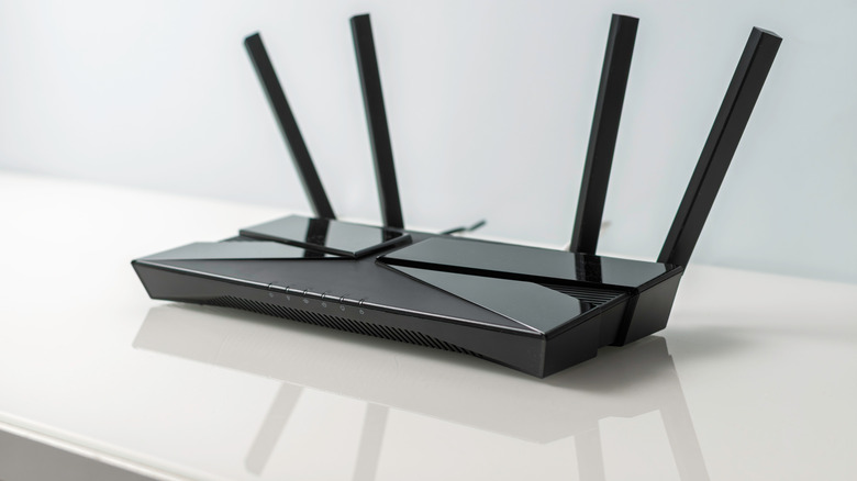 Black Wi-Fi router with antennas on a white surface.