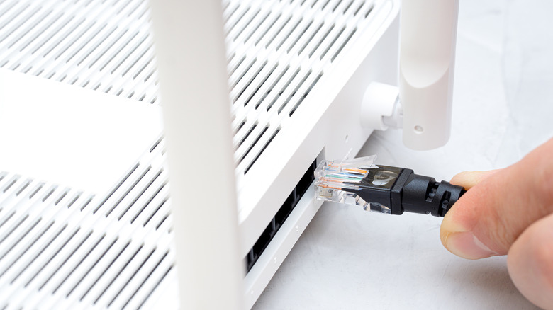 A hand plugging an Ethernet cable into a Wi-Fi router.