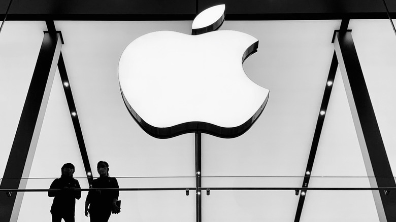 Apple logo on the front of an Apple Store, with two people in silhouette below.