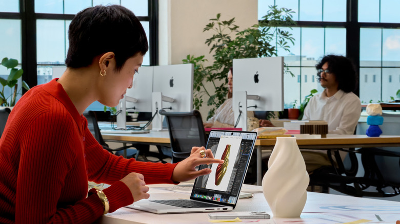 A person touching a laptop screen in an office.