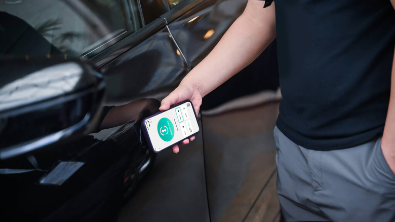 Someone holding a smartphone near a car door to unlock it over NFC.