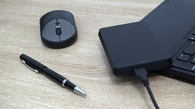 Um HDD externo em um laptop, pr&oacute;ximo a uma caneta e um mouse.