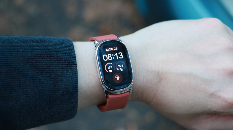 A Fitbit Edge with a narrow maroon band and silver lugs on a person's wrist.
