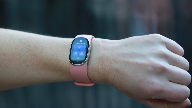 A Fitbit Edge with a pink band on a person's wrist, showing the Quick Start tile.