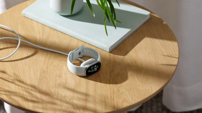 A Fitbit Edge charging on a side table.