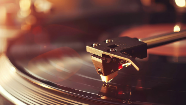 A close up shows a record player's cartridge lowered down upon a vinyl record as soft, warm light comes down from a nearby window.