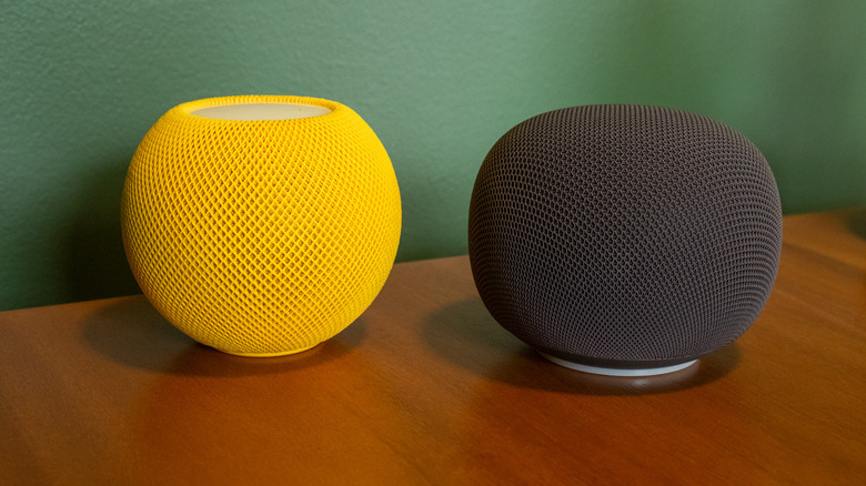The Google Home Speaker next to a yellow Apple HomePod mini.