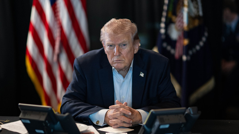 President Trump sits in front of two phones, with two US flags behind him.
