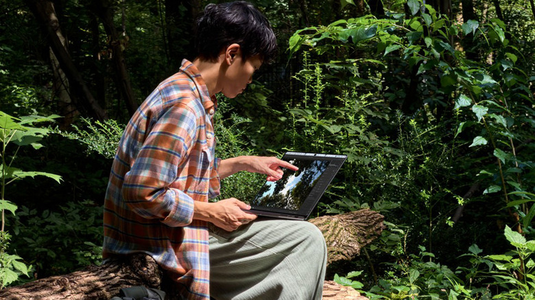 A man uses his finger to touch a MacBook Pro's screen.