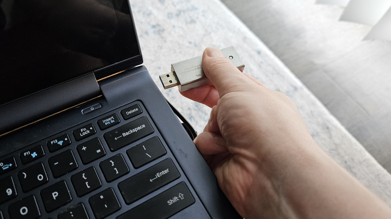 A hand plugging a Kingston USB drive into a Samsung laptop.