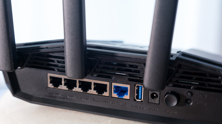 A close up of a black ASUS router shows the factory reset button, as well as several inputs.