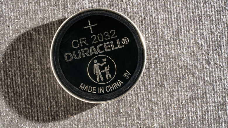 A black Duracell CR2032 coin-cell battery resting on textured gray fabric.